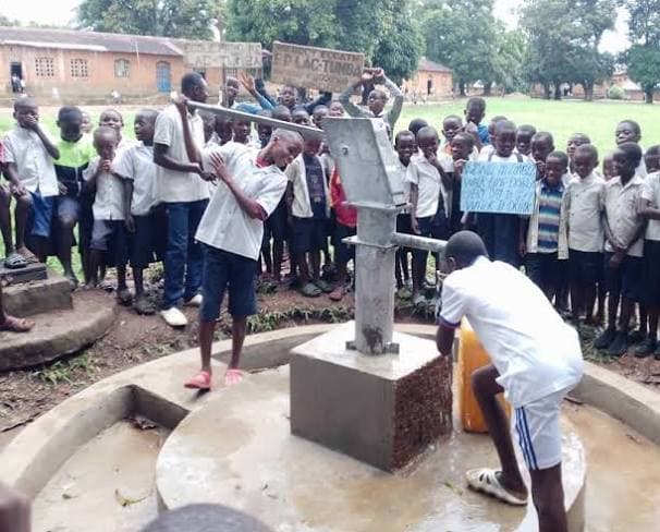Children crowded around a deteriorating borehole pump at a school